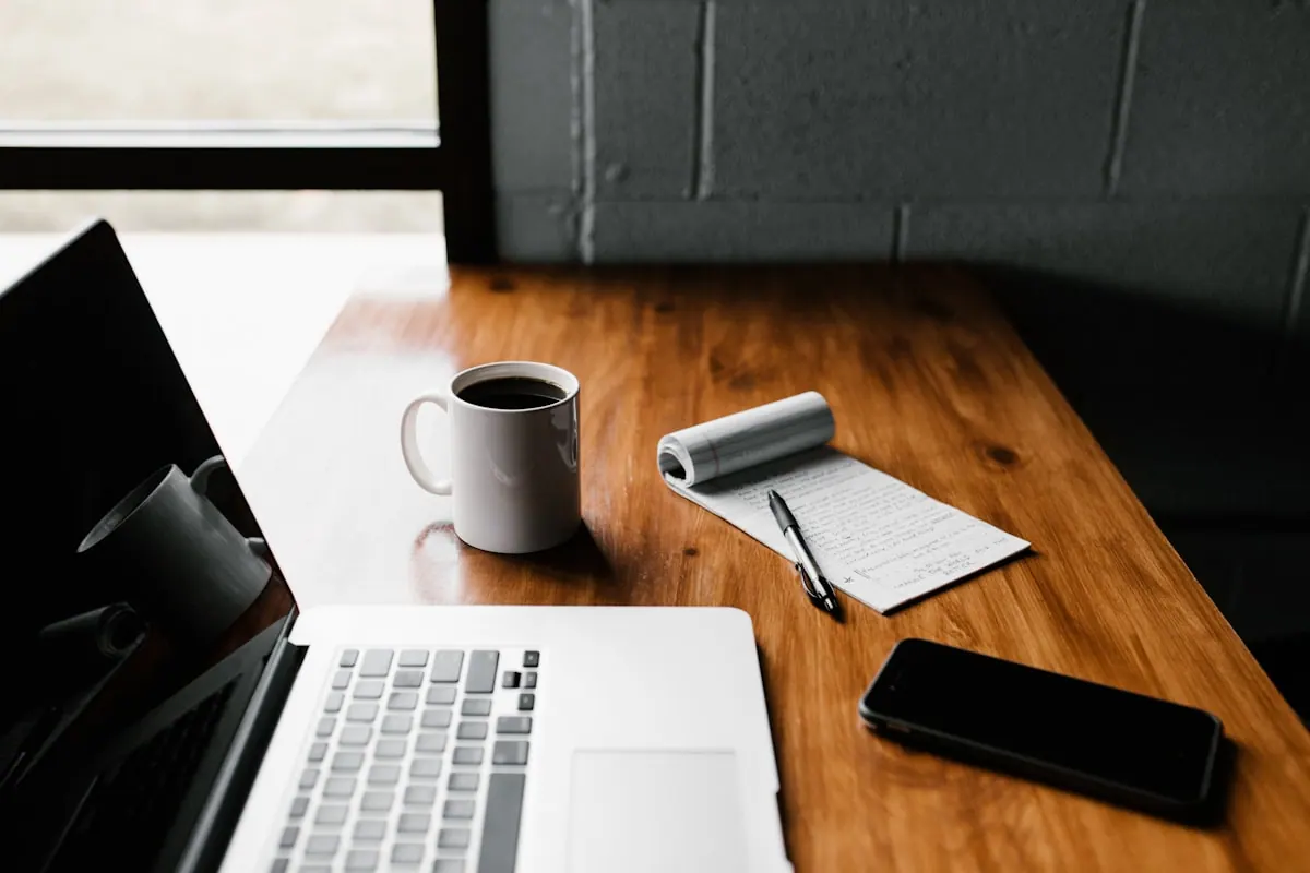 Ordinateur portable, téléphone, café et bloc-notes sur un bureau en bois
