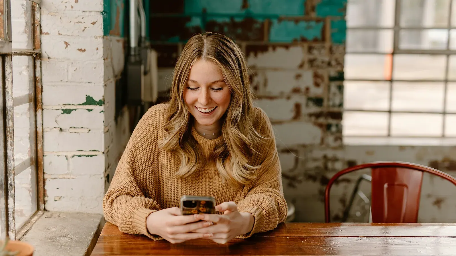 Woman smiling at a message on her phone in a sunlit cafe